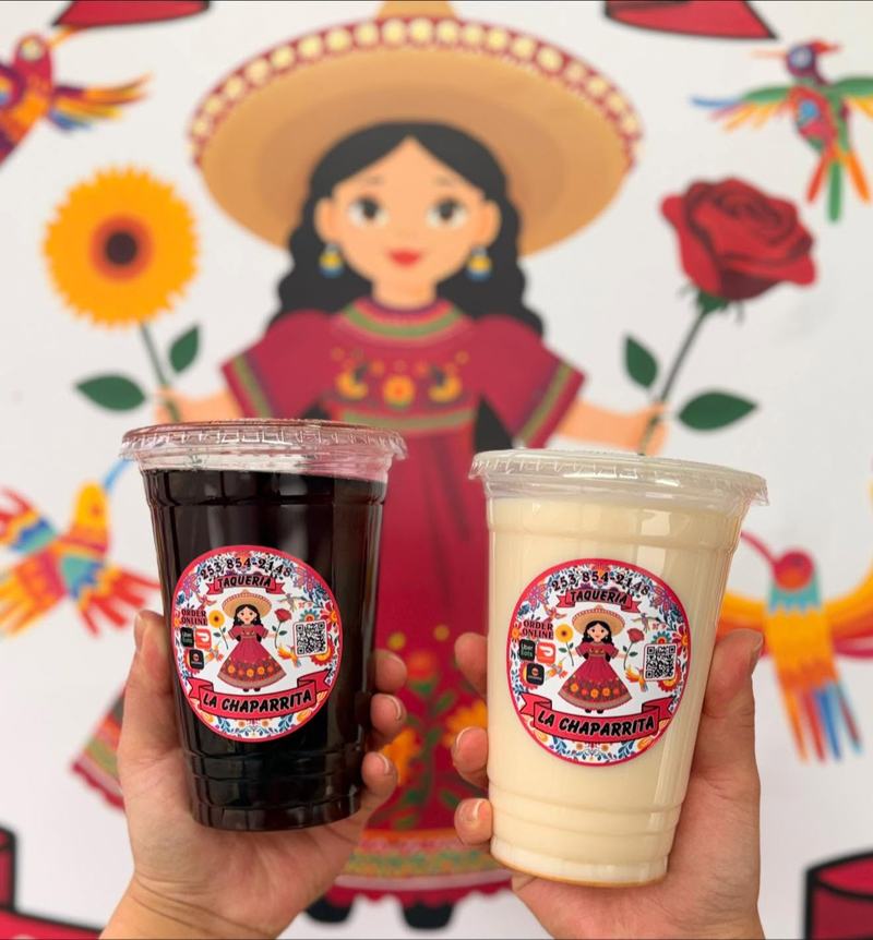 Two La Chaparrita drink cups held up in front of the truck's floral banner, one dark red and one creamy white.