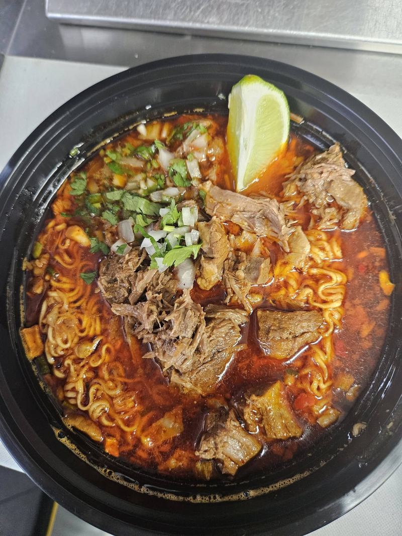 Birria ramen: noodles and shredded beef in a red chile broth, topped with chopped onion, cilantro and a wedge of lime.