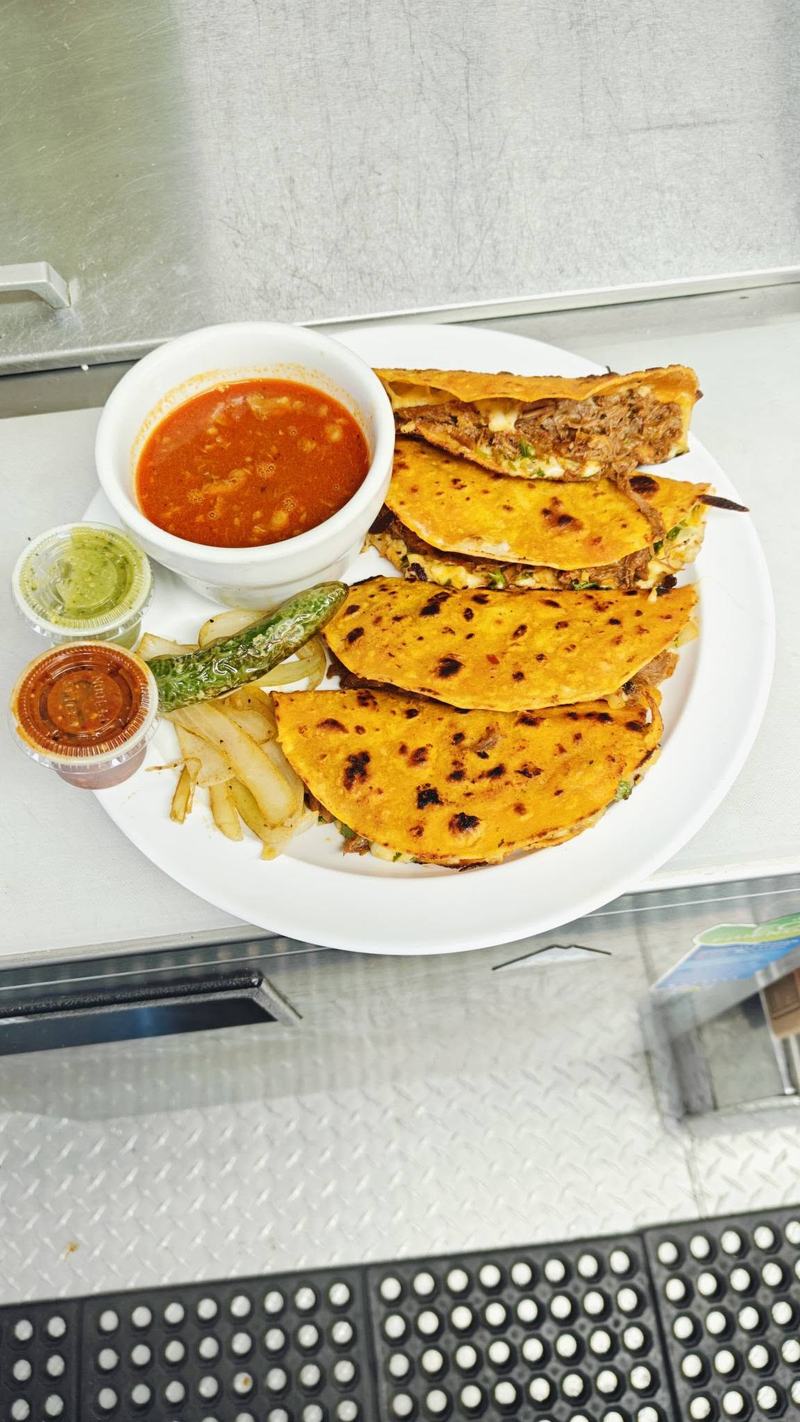 Crisped quesabirria tacos with melted cheese, served with a bowl of consomé, fries, a roasted chile and two salsas.