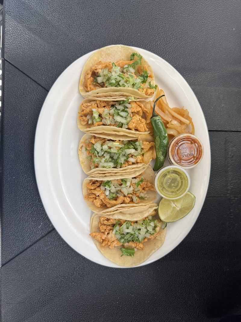 Five soft corn tacos topped with chopped onion and cilantro, served with lime, a roasted jalapeño and red and green salsas.