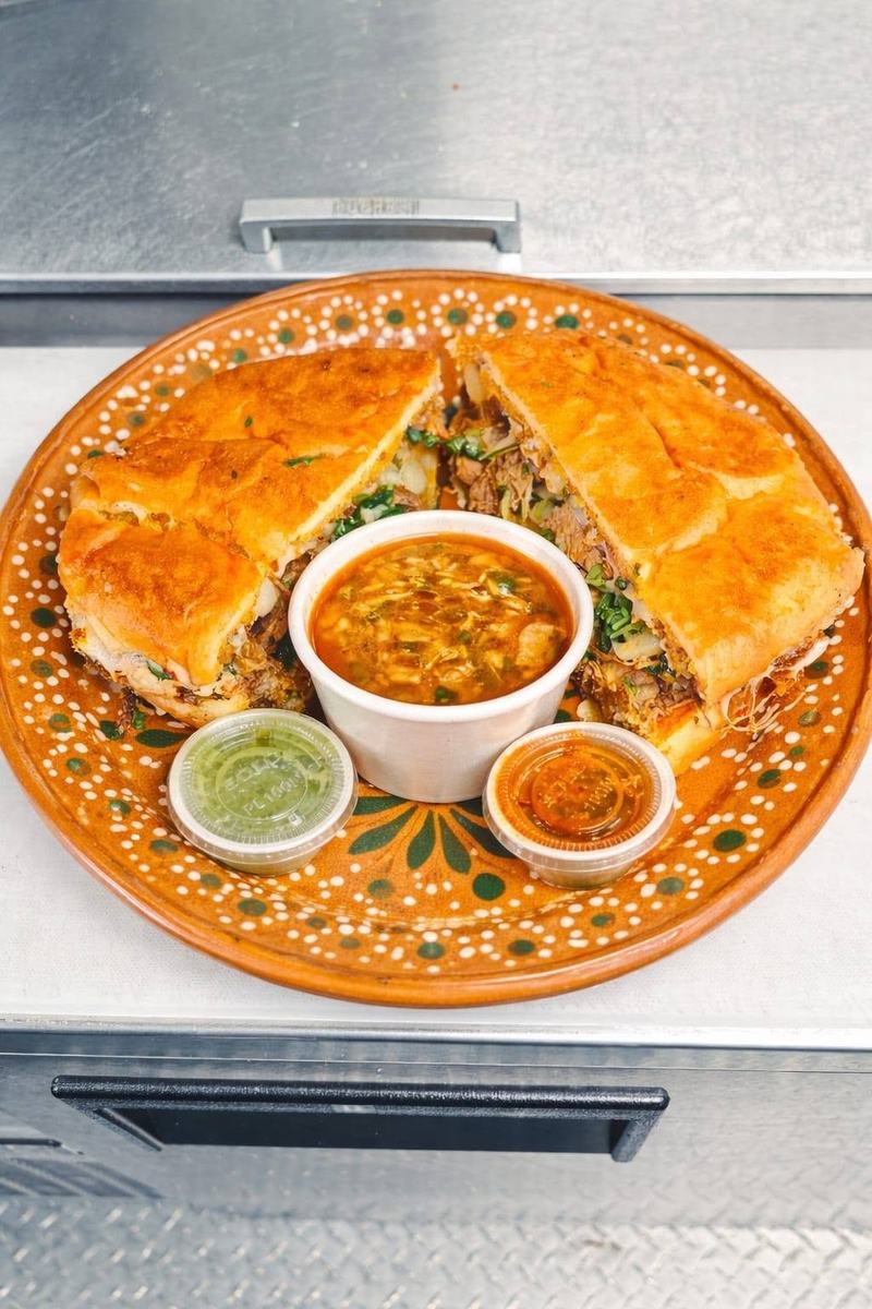 A torta cut into quarters on a painted clay plate, served with a cup of consomé and two salsas.