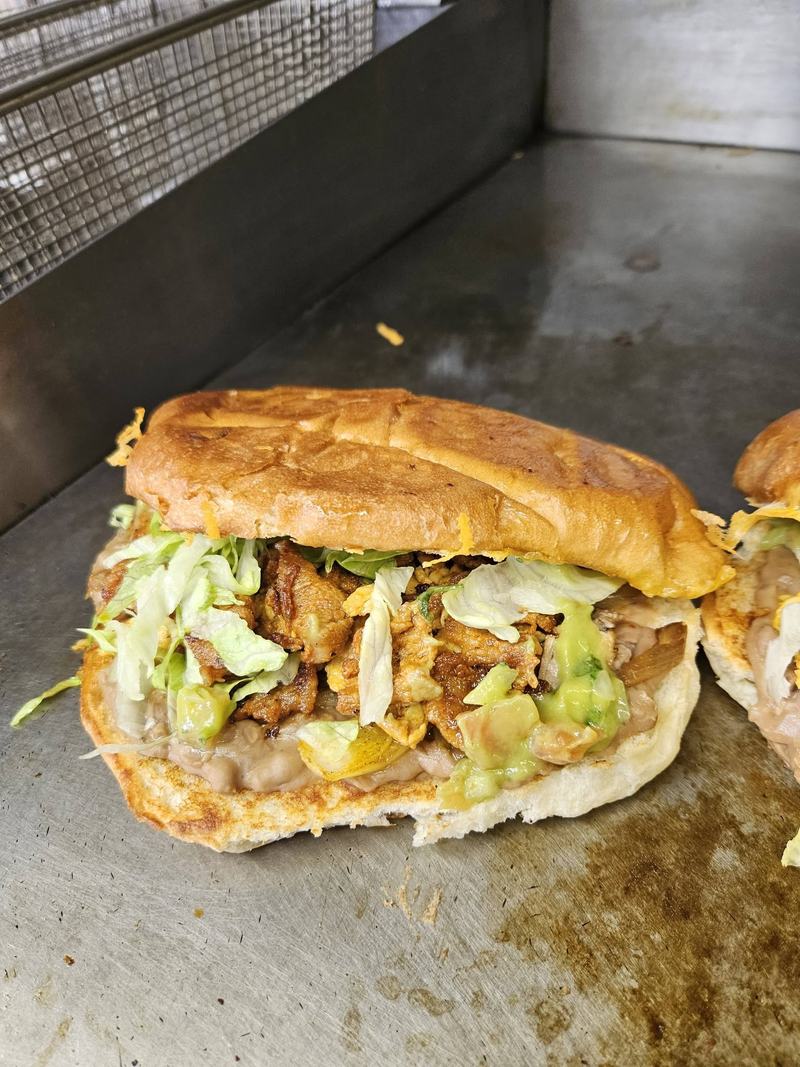 A torta on the griddle, layered with beans, meat, shredded lettuce and guacamole.